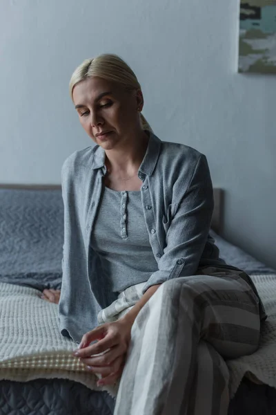 Sad blonde woman with menopause sitting on bed at home — Stock Photo