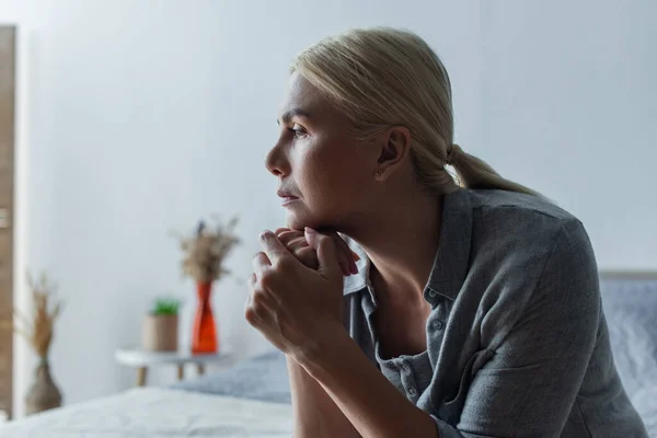 Side view of worried blonde woman with menopause looking away in bedroom — Photo de stock