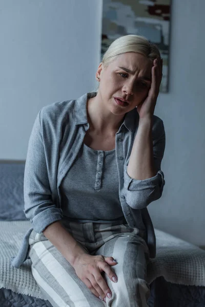 Засмучена блондинка з менопаузою страждає від головного болю в спальні — стокове фото