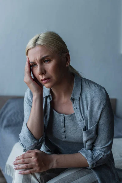 Mulher loira exausta com menopausa sofrendo de dor de cabeça no quarto — Fotografia de Stock