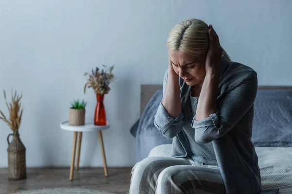 Exhausted woman with menopause suffering from headache while sitting in bedroom — Stock Photo