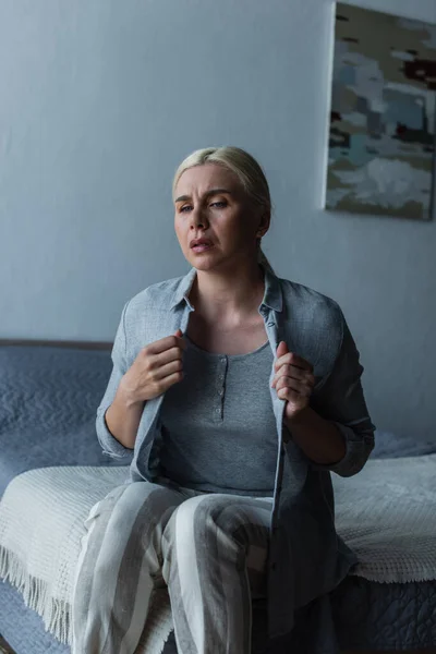 Mulher loira com menopausa sofrendo de calor e cardigan tocando no quarto — Fotografia de Stock