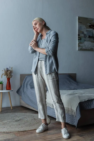 Full length of tired woman with menopause standing and touching forehead in bedroom — Stock Photo