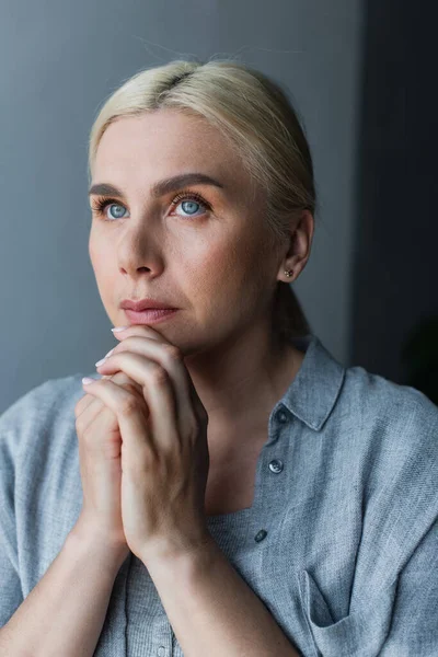 Portrait of blonde woman with blue eyes and clenched hands praying at home — Stockfoto