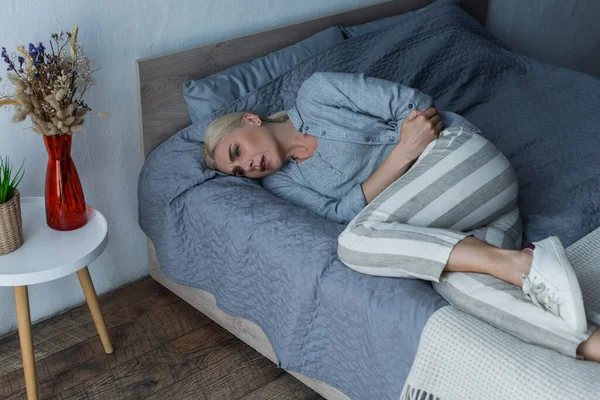 Donna frustrata con menopausa che soffre di dolore addominale e sdraiata sul letto — Foto stock