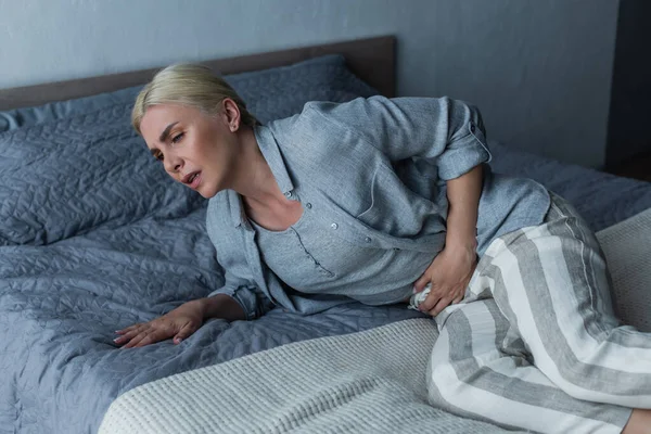 Tired blonde woman with menopause suffering from abdominal pain in bedroom — Foto stock