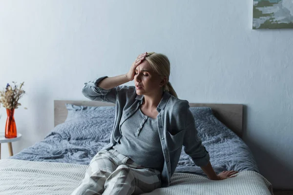 Расстроенная блондинка с менопаузой страдает от мигрени в спальне — стоковое фото