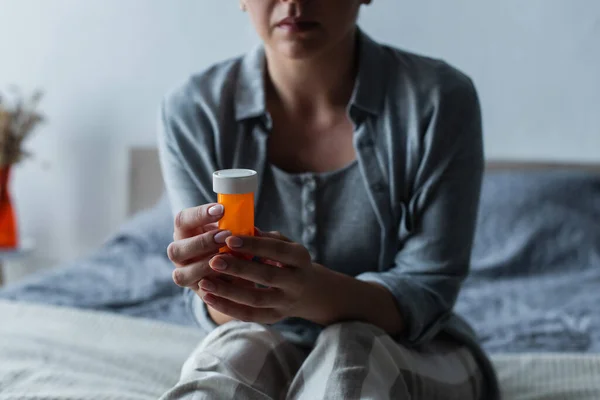 Ausgeschnittene Ansicht einer Frau mit Wechseljahren, die eine Flasche mit Pillen in der Hand hält und auf dem Bett sitzt — Stockfoto