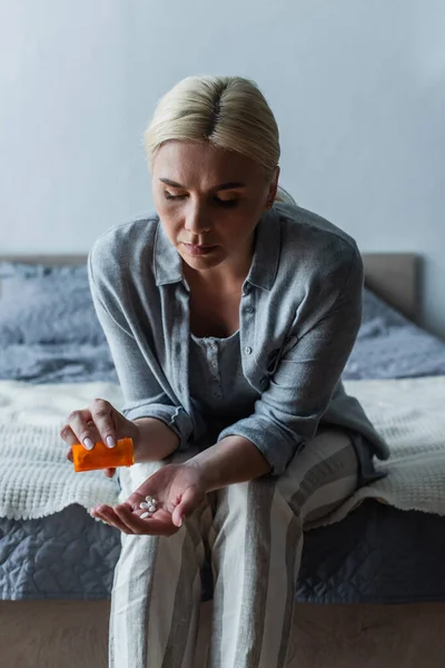 Mujer rubia disgustada con la menopausia sosteniendo la botella y vertiendo pastillas en la mano - foto de stock
