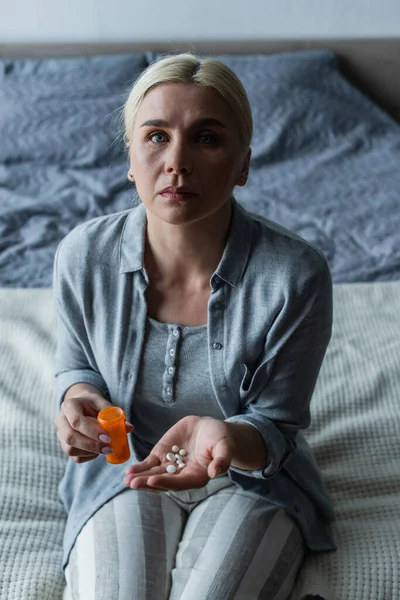 Расстроенная блондинка с менопаузой держа в руках бутылку и таблетки — стоковое фото