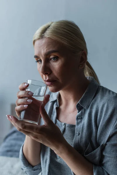 Sad blonde woman with menopause drinking fresh water from glass — Photo de stock