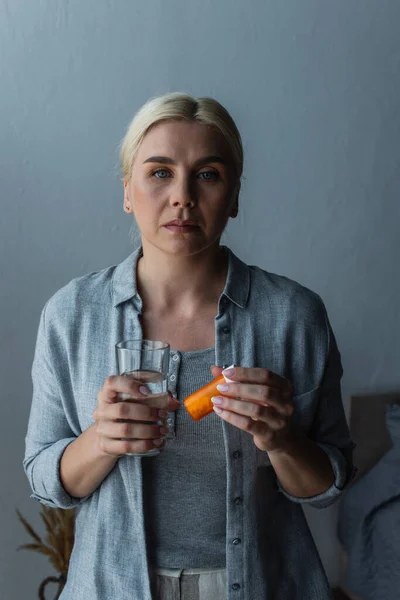 Mulher loira com menopausa segurando vidro de água e garrafa com medicação — Fotografia de Stock