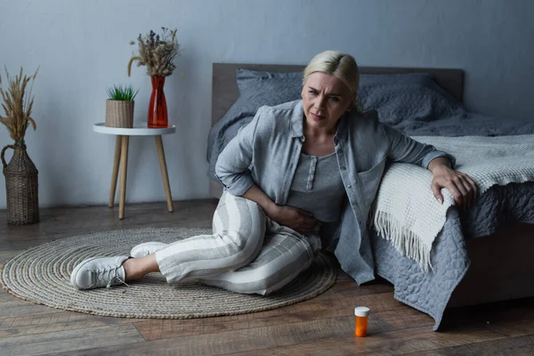 Mulher com menopausa sentada perto da cama enquanto sofre de dor abdominal — Fotografia de Stock