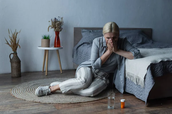 Femme ménopausée assise près du lit tout en couvrant le visage et souffrant de douleurs abdominales — Photo de stock