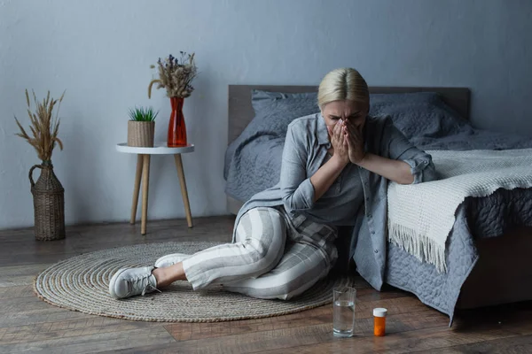 Woman with menopause sitting near bed while covering face and suffering from abdominal pain — Foto stock