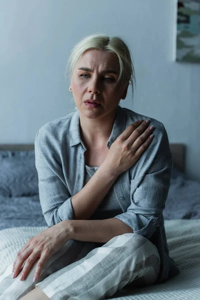 Exhausted blonde woman sitting in bedroom during menopause - foto de stock