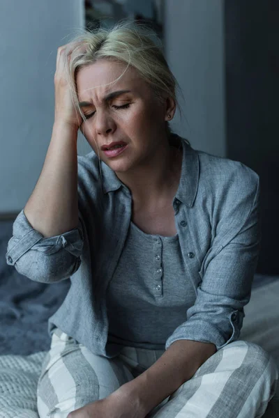 Exhausted blonde woman touching head and having migraine during menopause — Stock Photo