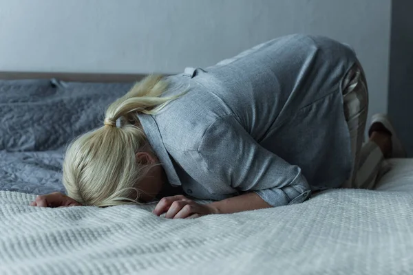 Blonde woman lying on bed while feeling pain in stomach during menopause - foto de stock