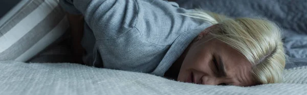 Femme blonde allongée sur le lit tout en ressentant une douleur dans l'estomac pendant la ménopause, bannière — Photo de stock