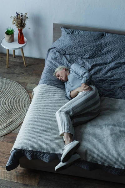 High angle view of blonde woman lying on bed while having stomach ache during menopause - foto de stock