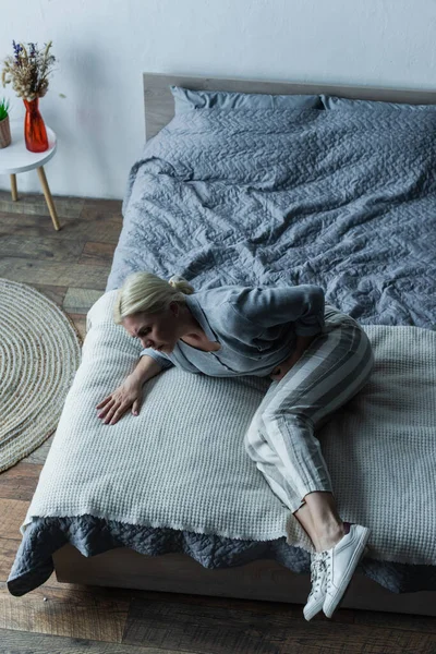 High angle view of frustrated woman lying on bed while feeling pain in stomach during menopause — Fotografia de Stock