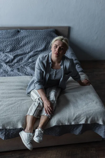 High angle view blonde woman sitting on bed while feeling pain in stomach during menopause — Foto stock