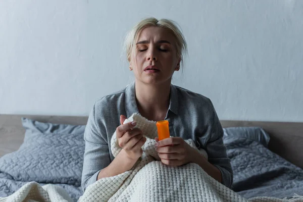 Traurige Frau mit Höhepunkt sitzt im Bett und hält Flasche mit Schmerzmitteln in der Hand — Stockfoto
