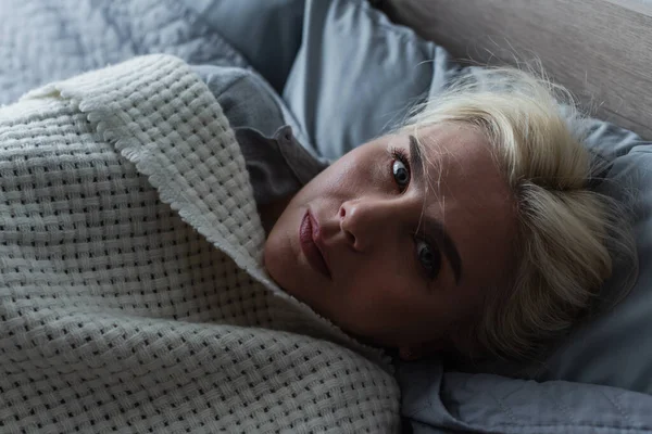 Top view of depressed blonde woman with menopause lying under blanket in bed — Foto stock