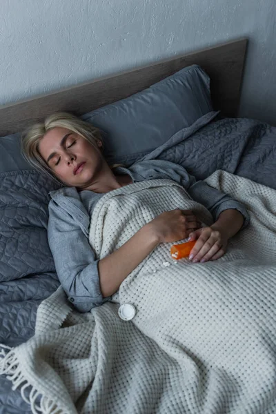 Vista de ángulo alto de la mujer rubia deprimida con la menopausia durmiendo cerca de píldoras en la cama - foto de stock