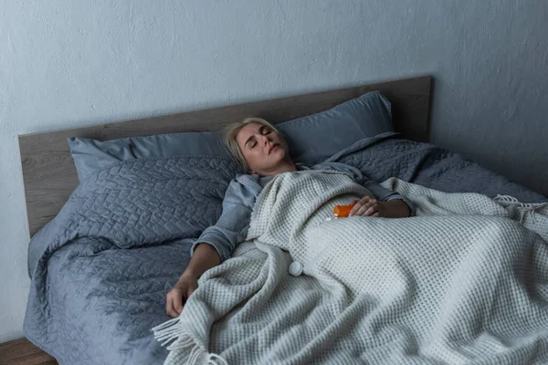 Mujer rubia deprimida con menopausia durmiendo cerca de pastillas en la cama - foto de stock