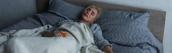 Mujer rubia deprimida con menopausia durmiendo cerca de pastillas en la cama, pancarta — Stock Photo