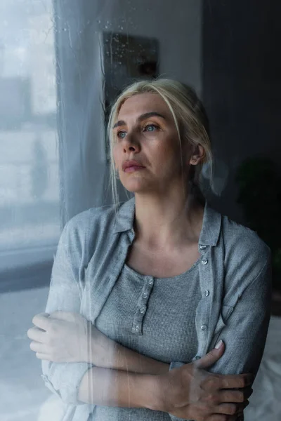 Depressed blonde woman looking at window with rain drops — Stockfoto