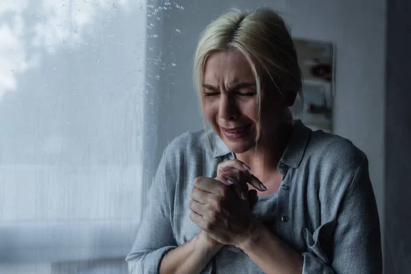 Mulher loira deprimida chorando atrás do vidro da janela com gotas de chuva — Fotografia de Stock