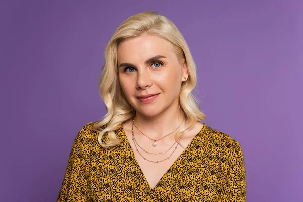 Happy and blonde woman in blouse looking at camera isolated on purple — Foto stock