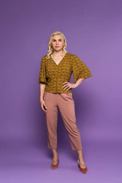 Full length of blonde woman in blouse posing with hand on hip on purple — Foto stock