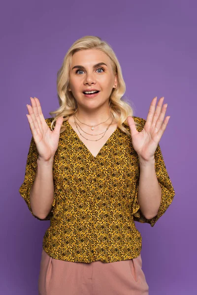 Amazed and blonde woman in blouse gesturing isolated on purple - foto de stock