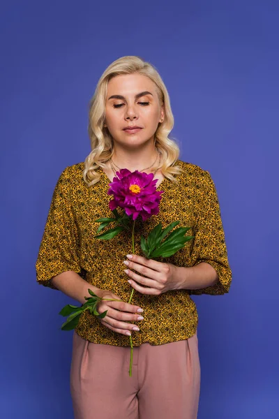 Blonde woman in blouse holding purple flower with green leaves isolated on violet — Stock Photo