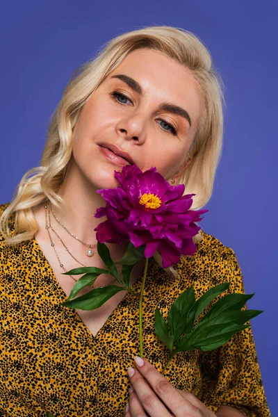 Mulher sonhadora com olhos azuis segurando flor roxa com folhas verdes isoladas em violeta — Fotografia de Stock