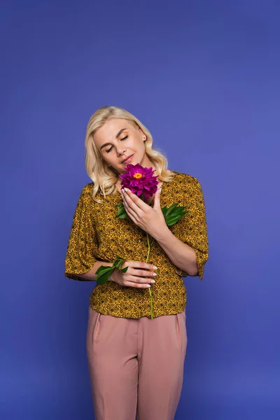 Блондинка в блузке держа цветок с зелеными листьями изолированы на фиолетовый — стоковое фото
