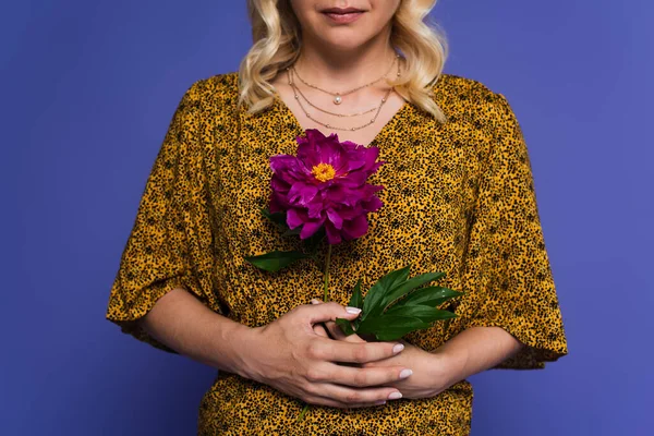 Cropped view of blonde woman in blouse holding purple flower with green leaves isolated on violet — Stock Photo