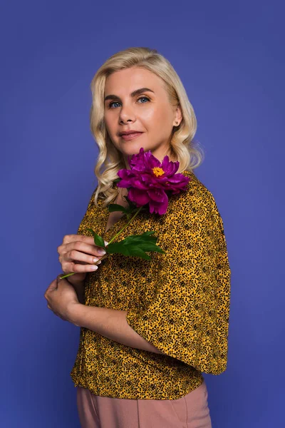 Blonde Frau mit blauen Augen, die Blume mit grünen Blättern auf Veilchen isoliert hält — Stockfoto