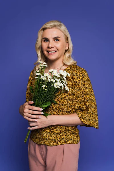 Mulher feliz em blusa segurando buquê de flores brancas com folhas verdes isoladas em violeta — Fotografia de Stock