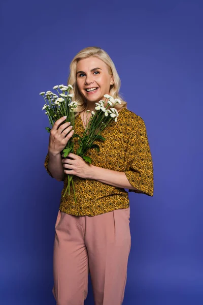 Gioiosa donna in camicetta che tiene mazzo di fiori bianchi con foglie verdi isolate su viola — Foto stock