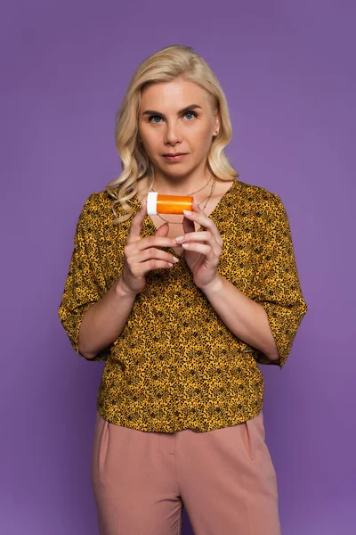 Blonde woman with menopause holding bottle with pills isolated on purple - foto de stock