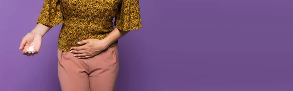 Cropped view of woman with stomach ache holding pills isolated on purple, banner — Stock Photo