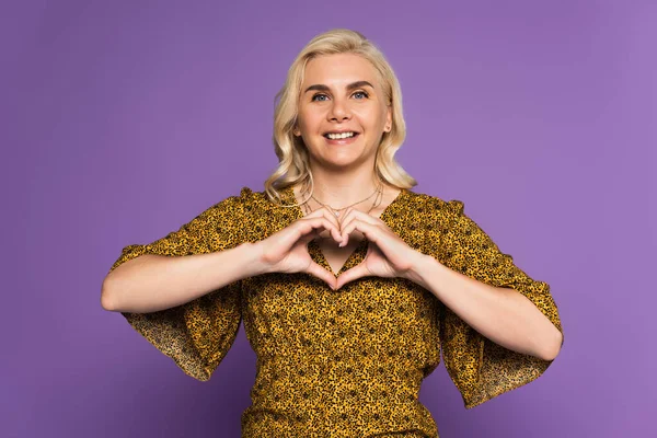 Счастливая блондинка показывает знак сердца с руки изолированы на фиолетовый — стоковое фото