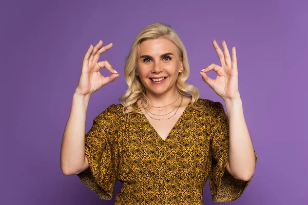 Joyful blonde woman with menopause smiling and showing ok with hands isolated on purple — Stockfoto