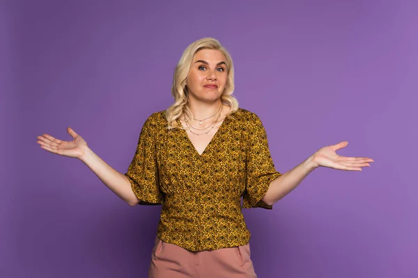 Confused blonde woman with menopause showing shrug gesture on purple - foto de stock