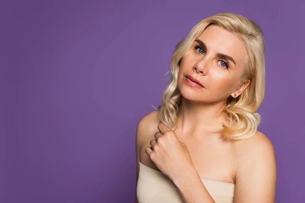 Pretty blonde woman with bare shoulders looking at camera isolated on purple — Foto stock