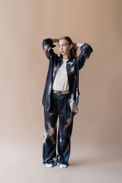 Pleine longueur de femme en costume dégradé et chaussettes blanches posant avec les mains derrière la tête sur fond beige — Photo de stock